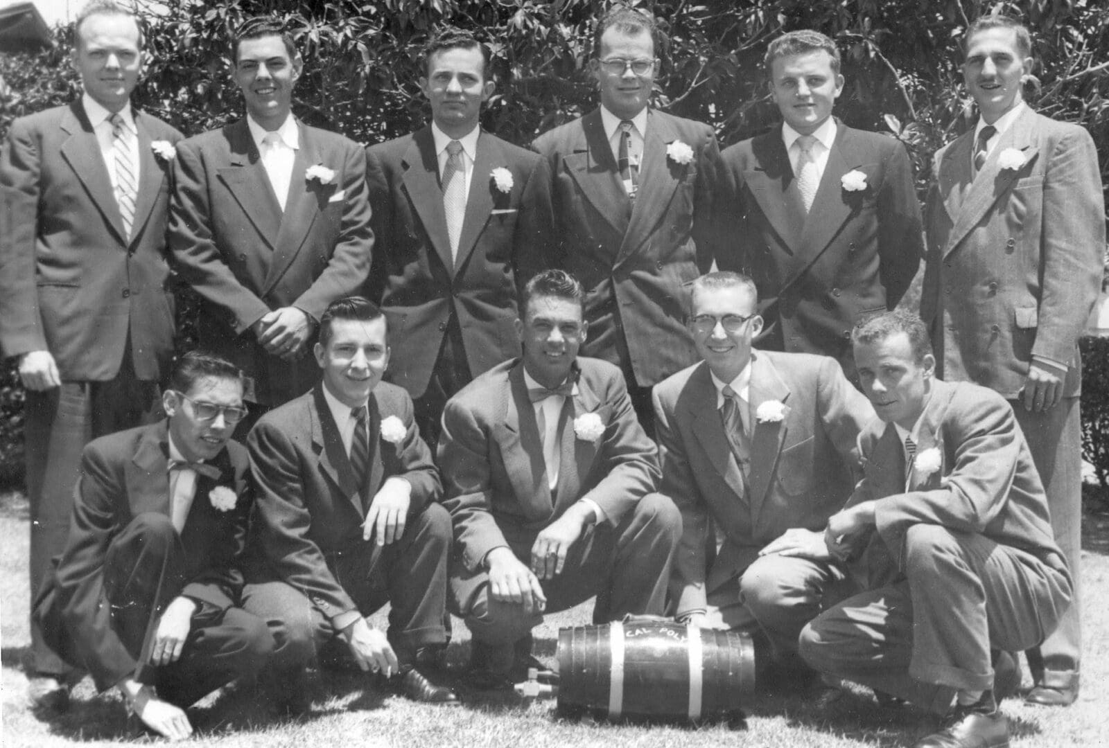 A group of men in suits and ties sitting on the ground.