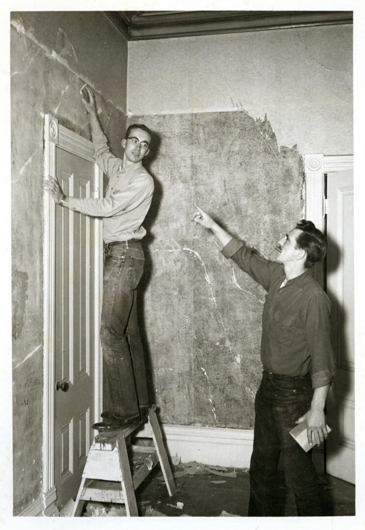 Two men are working on a wall.