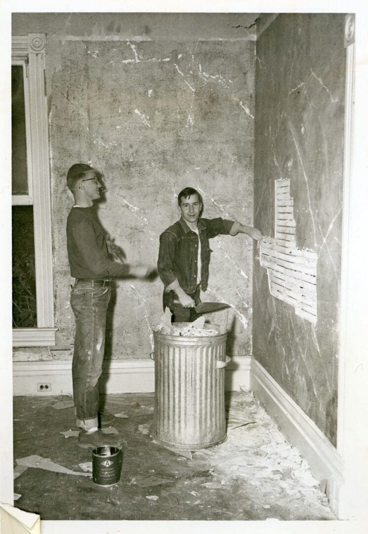 Two men are standing in front of a trash can.