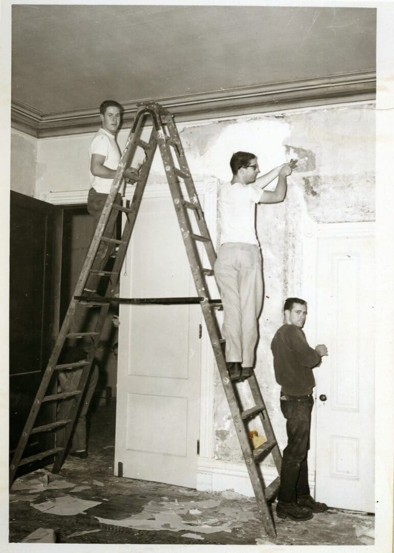 Three men are standing on a ladder and painting the wall.