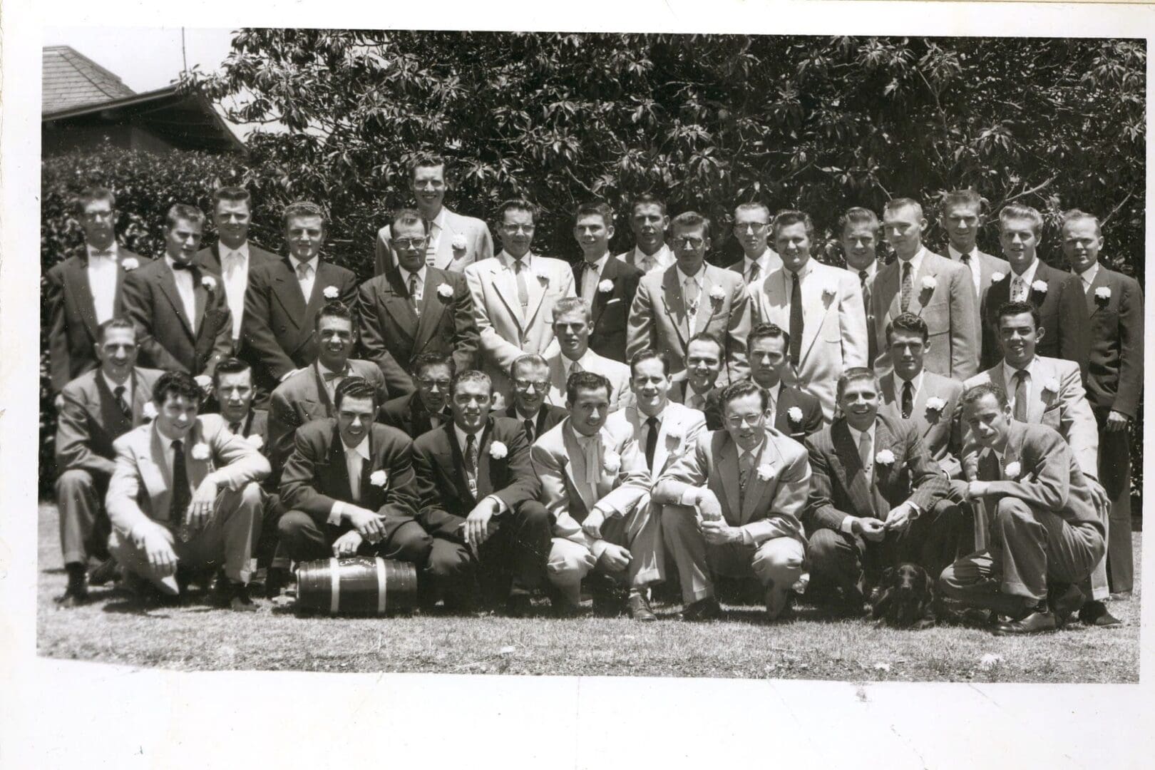 A group of men in suits and ties sitting on the ground.
