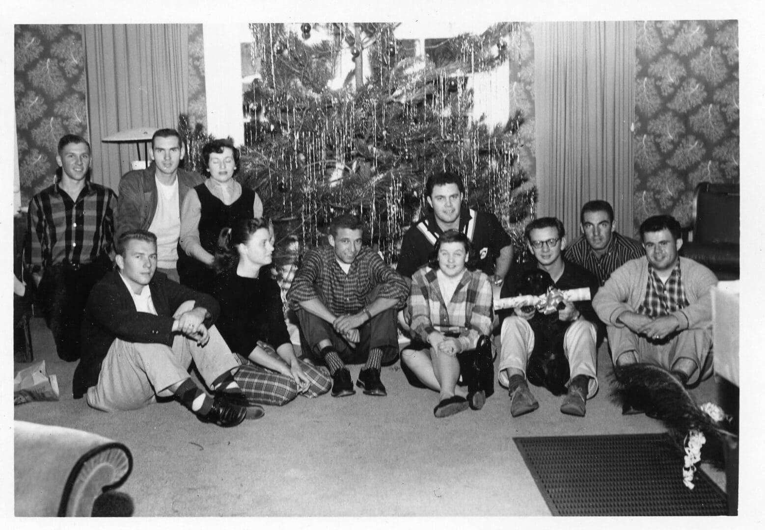 A group of people sitting around in front of a christmas tree.