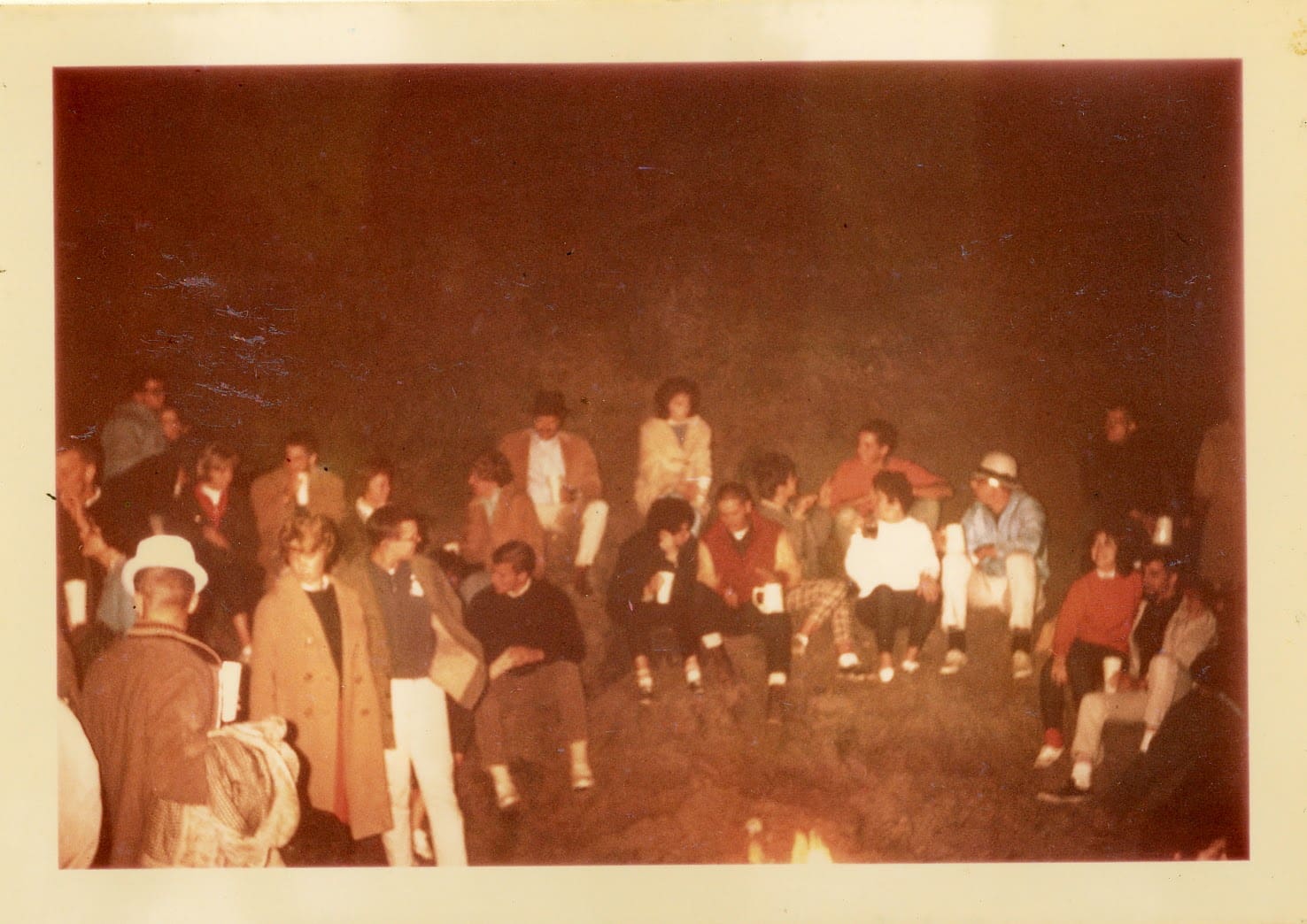 A group of people sitting around in front of fire.