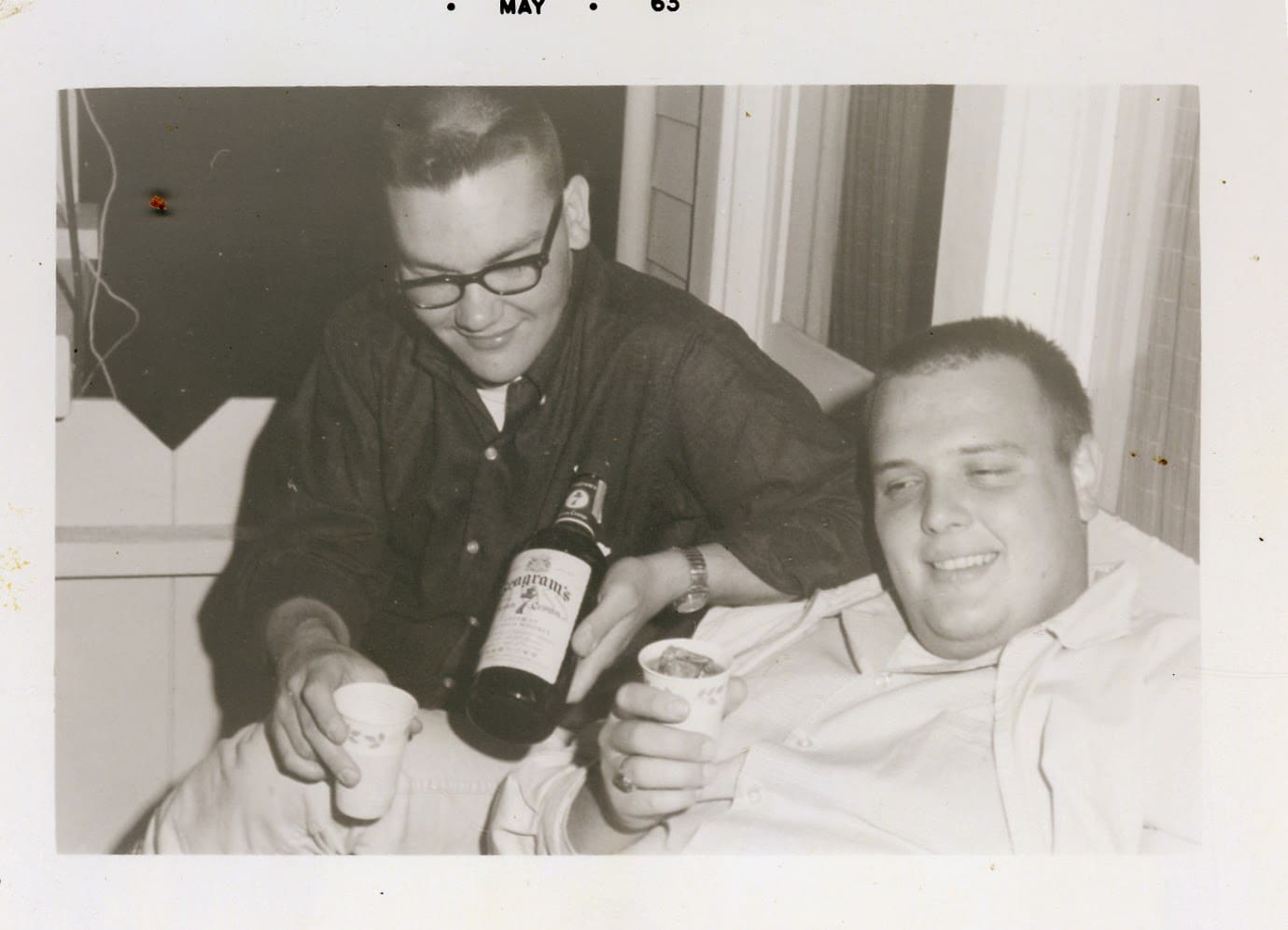 A man sitting next to another man holding a bottle of wine.