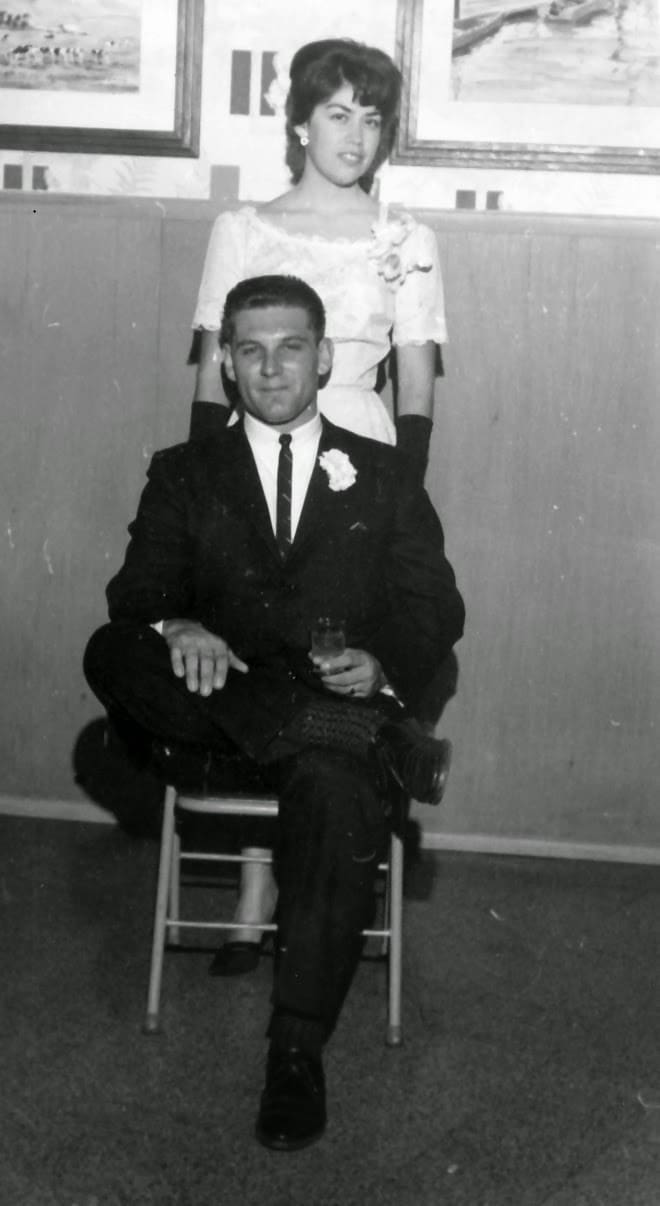 A man sitting on the back of a chair next to a woman.