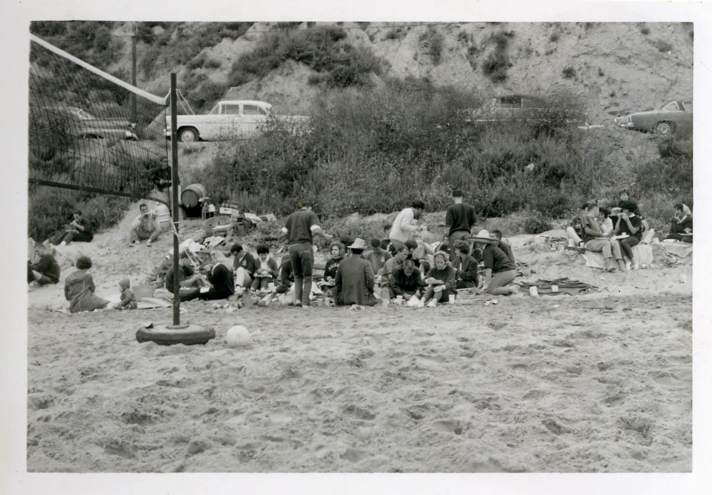 A group of people sitting on top of a sandy beach.