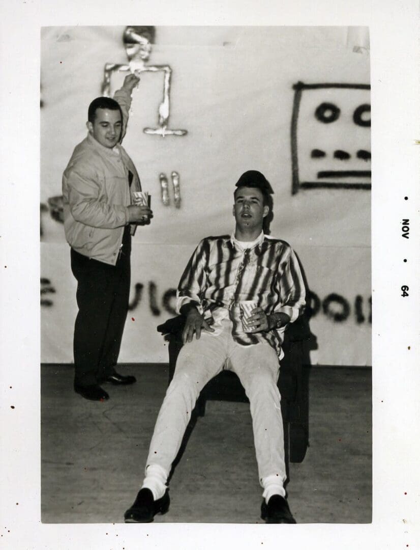 Two men sitting in a room with a wall mural behind them.