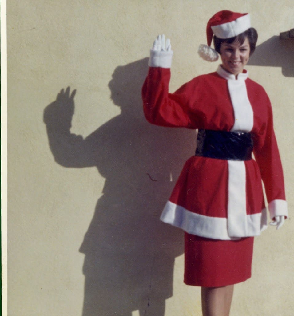 A woman in a santa suit waving to the camera.