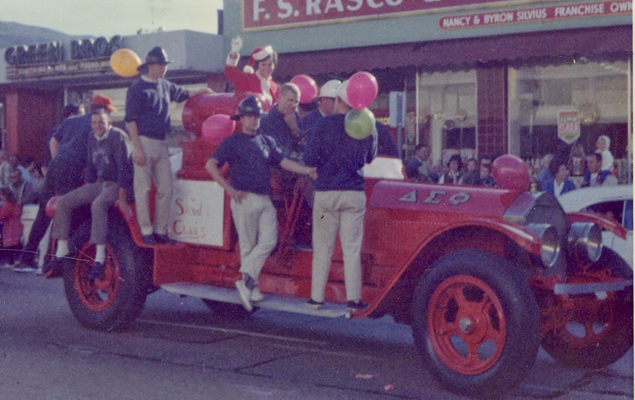 A group of men riding on the back of an old fire truck.