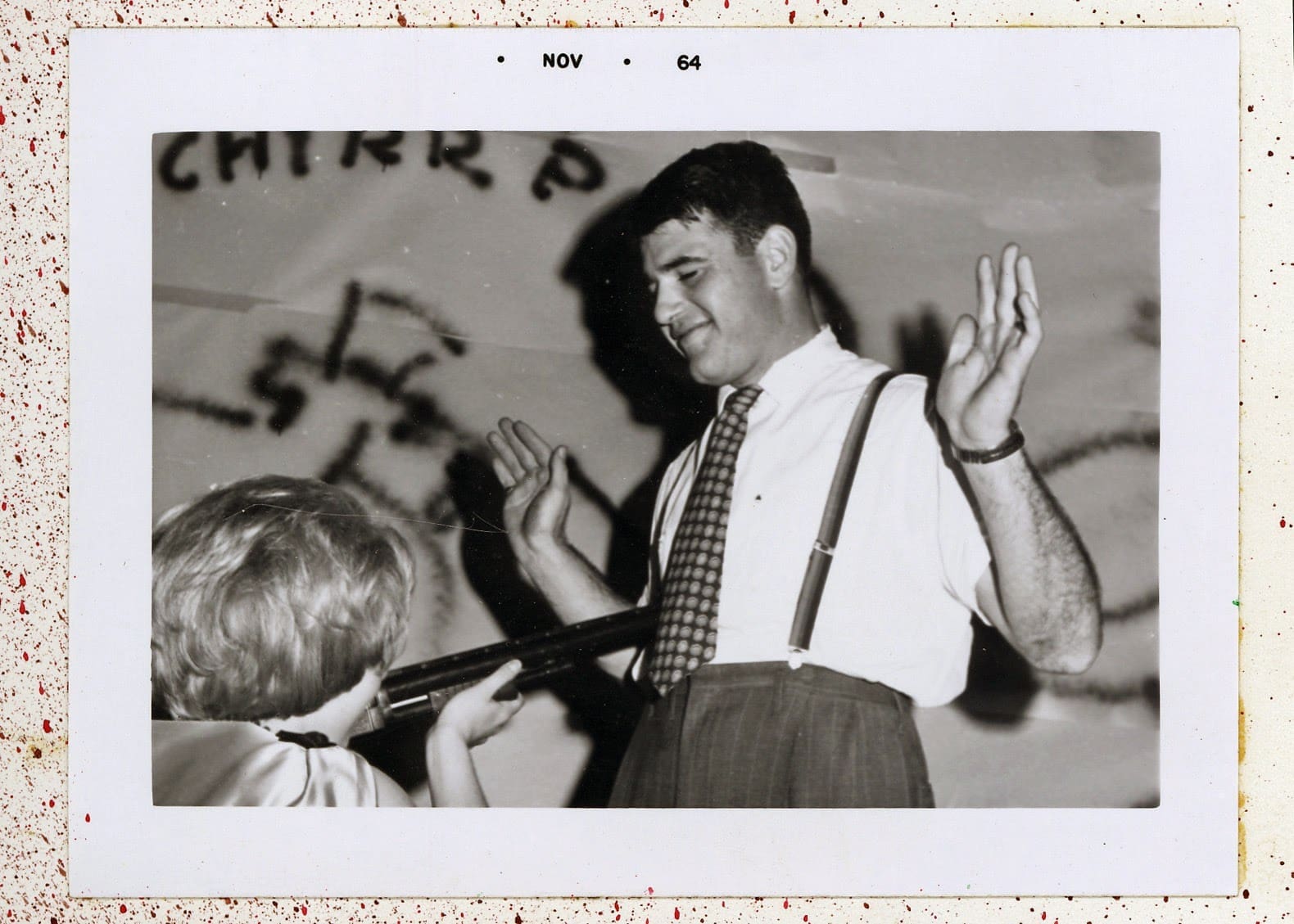 A man in a tie and suspenders is holding his hands up.