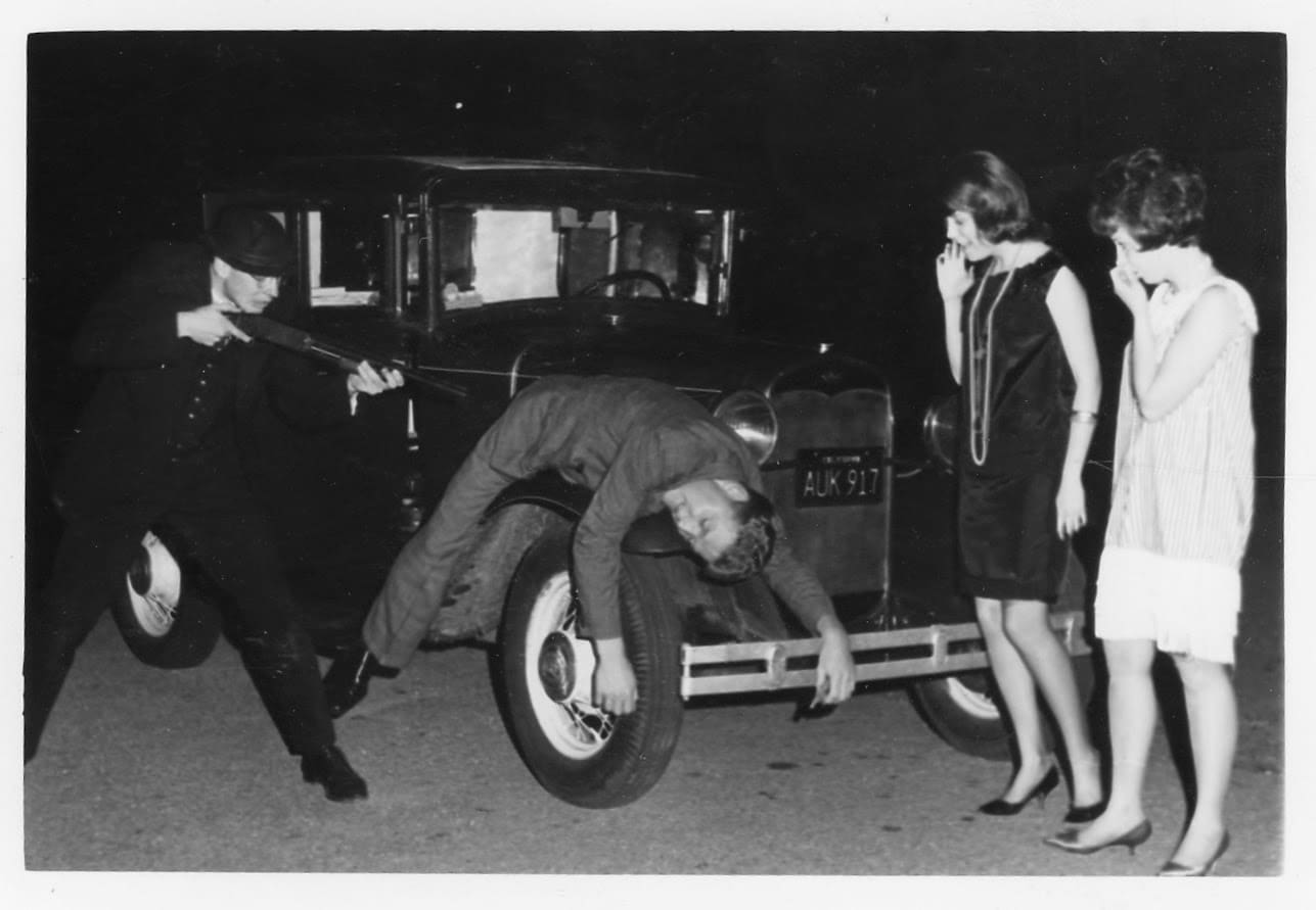 A man is doing something with the back of an old car.