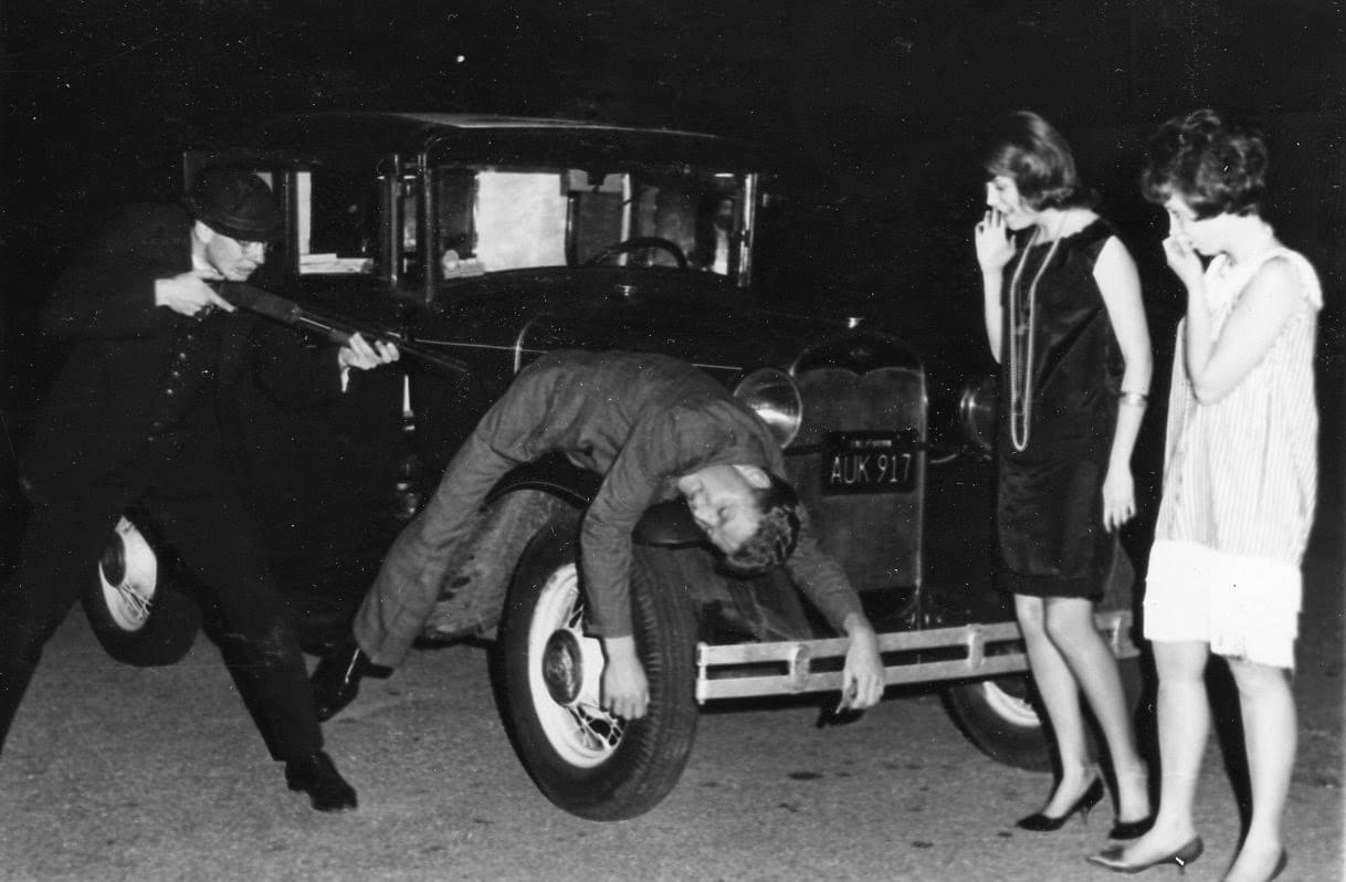 A man is doing something with the tires of an old car.
